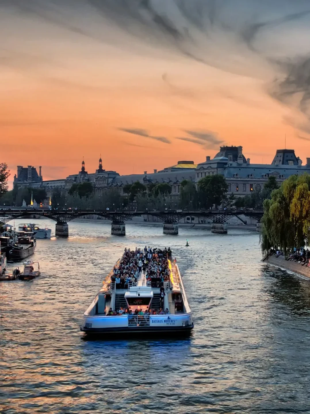 Bateau-mouche faisant l'escapade Croisière sur la Seines au coucher du soleil à Paris avec le musée du Louvre en arrière-plan.