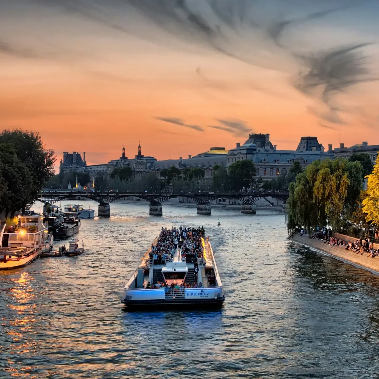 Bateau-mouche faisant l'escapade Croisière sur la Seines au coucher du soleil à Paris avec le musée du Louvre en arrière-plan.