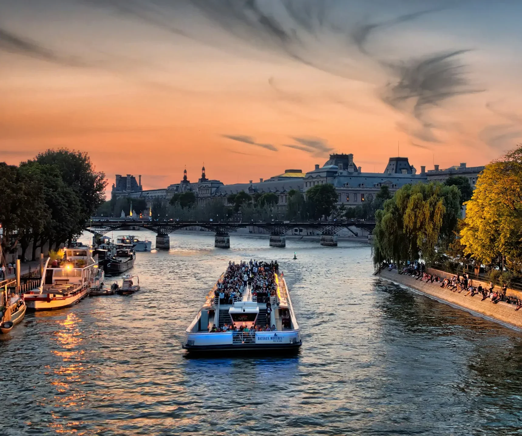 Bateau-mouche faisant l'escapade Croisière sur la Seines au coucher du soleil à Paris avec le musée du Louvre en arrière-plan.