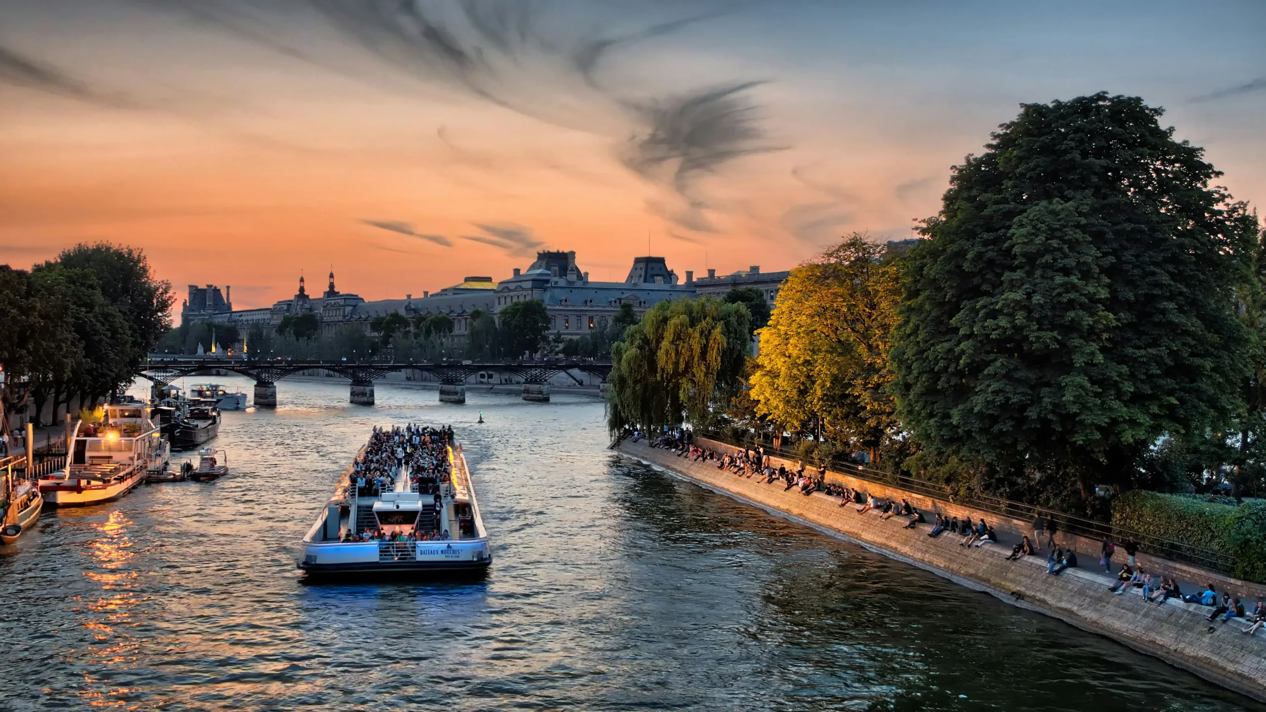 Bateau-mouche faisant l'escapade Croisière sur la Seines au coucher du soleil à Paris avec le musée du Louvre en arrière-plan.